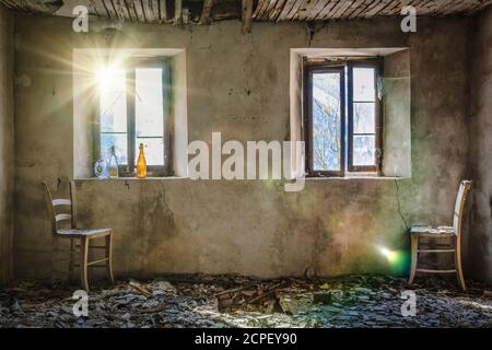 Staubiger Raum eines alten verlassenen Hauses, zwei Strohstühle, zwei Fenster und das Licht, das durch das Glas filtert Stockfoto