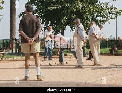 Petanque Spiel auf der Promenade. Der Spieler zeigt auf das Ziel. Das Publikum beobachtet mit zurückgefalteten Armen. Seriöse, respektable Rentner. Stockfoto