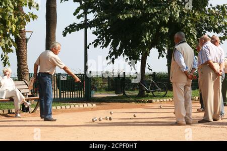 Petanque Spiel auf der Promenade. Der Spieler zeigt auf das Ziel. Das Publikum beobachtet mit zurückgefalteten Armen. Seriöse, respektable Rentner. Stockfoto