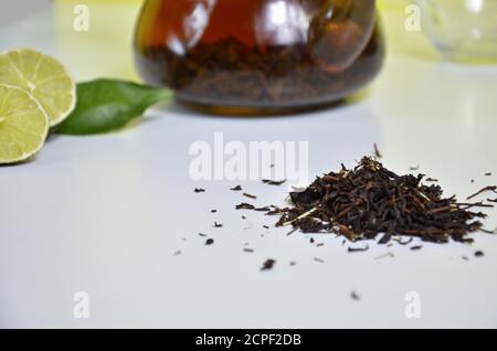 Transparente Teekanne mit schwarzem Tee, trockener Tee auf dem Tisch, Bergamottscheiben oder Zitrone oder Limette auf weißem Hintergrund Stockfoto