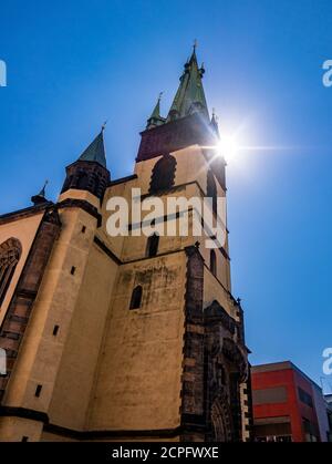 Schiefer Turm der Kirche mit der Sonne wirft Strahlen über seine Spitze. Kirche Mariä Himmelfahrt - Usti nad Labem / Tschechische Republik Stockfoto