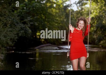 Junge Frau in rotem Kleid auf einer Schaukel Stockfoto