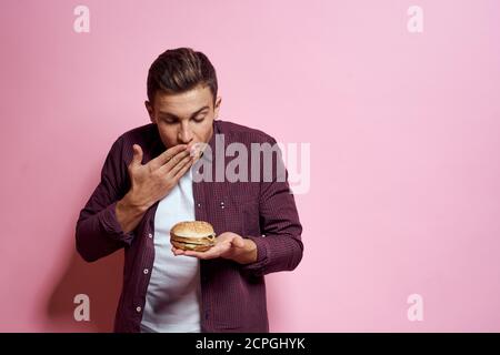 Hungrige Mann mit Hamburgern in den Händen Fast-Food-Diät-Lebensmittel Emotionen rosa Hintergrund Stockfoto