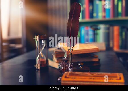 Alte Federkiel, Bücher und Vintage Tintenfass auf Holztisch im alten Büro vor dem Hintergrund des Bücherregals. Konzeptueller Hintergrund zur Geschichte, ed Stockfoto