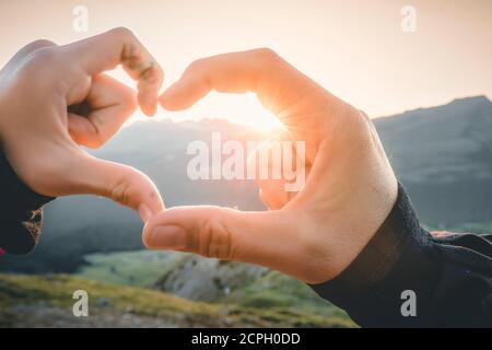 Mutter und Tochter, Frau und Mädchen verbinden sich mit den Händen und schaffen die Form des Herzens mit der untergehenden Sonne Stockfoto