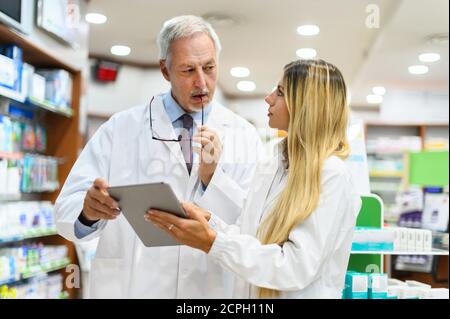 Zwei Apotheker sprechen, während sie in ihrem Geschäft an einer Tablette arbeiten Stockfoto