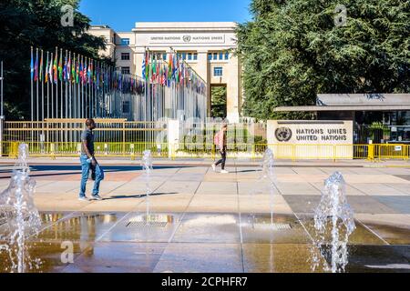 Menschen, die am Eingang des Nationenpalastes, dem Sitz des Büros der Vereinten Nationen in Genf, Schweiz, und der Allee der Flaggen vorbei gehen. Stockfoto