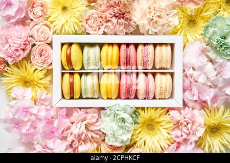 Runde schöne Süßigkeiten Makkaroni in einer festlichen Box mit Blumen auf einem Blumenhintergrund. Stillleben mit Makkaroni-Kuchen und verschiedenen Blumen. Stockfoto