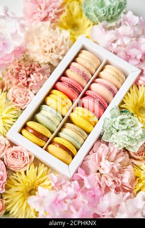 Runde schöne Süßigkeiten Makkaroni in einer festlichen Box mit Blumen auf einem Blumenhintergrund. Stillleben mit Makkaroni-Kuchen und verschiedenen Blumen. Stockfoto