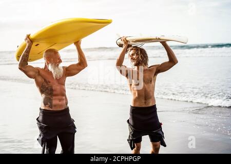 Mehrgenerationige Freunde, die am tropischen Strand surfen - Familienmitglieder haben Spaß am Extremsport - fröhliches älteres und gesundes Lifestyle-Konzept Stockfoto