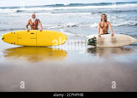 Mehrgenerationige Freunde, die am tropischen Strand surfen - Familienmitglieder haben Spaß am Extremsport - fröhliches älteres und gesundes Lifestyle-Konzept Stockfoto