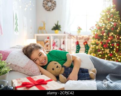 Frohe Weihnachten und frohe Feiertage! Nettes kleines Kind Mädchen schlafen im Bett in der Nähe von Baum zu Hause. Stockfoto