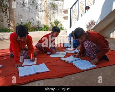 DISTRIKT KATNI, INDIEN - 13. JANUAR 2020: Indische Dorfschulkinder schreiben zusammen im offenen Innenhof. Stockfoto