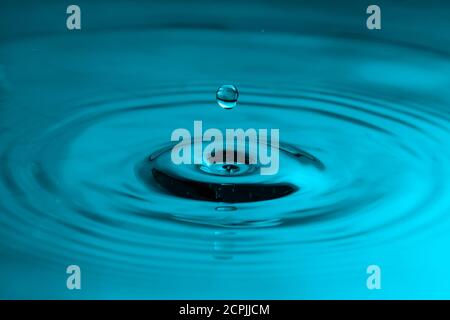 Perfekter Wassertropfen, der in glattes Wasser spritzt und Wellen verursacht Stockfoto