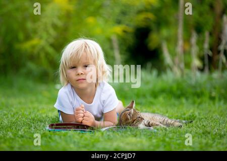 Cute blonde Kleinkind Kind, süßen Jungen, spielen im Garten mit kleinen Kätzchen, Buch lesen Stockfoto