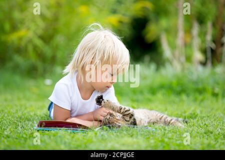 Cute blonde Kleinkind Kind, süßen Jungen, spielen im Garten mit kleinen Kätzchen, Buch lesen Stockfoto