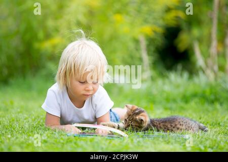 Cute blonde Kleinkind Kind, süßen Jungen, spielen im Garten mit kleinen Kätzchen, Buch lesen Stockfoto