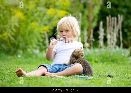 Cute blonde Kleinkind Kind, süßen Jungen, spielen im Garten mit kleinen Kätzchen, Buch lesen Stockfoto