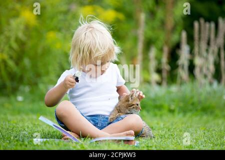 Cute blonde Kleinkind Kind, süßen Jungen, spielen im Garten mit kleinen Kätzchen, Buch lesen Stockfoto