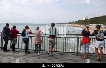 Die Leute beobachten Surfer im Meer vom Boscombe Pier in Dorset, das Met Office prognostiziert ein Wochenende von Òlargely trocken, hell und fineÓ Wetter, das Temperaturen bis zu 24C (75F) steigen sehen könnte. Stockfoto