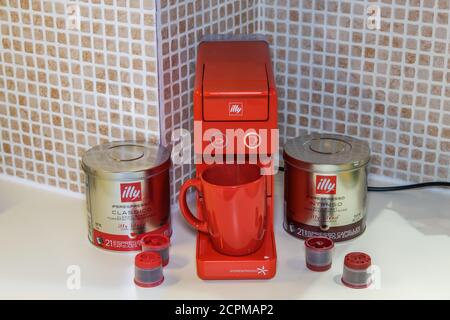 Automatische Illy iperespresso Maschine, um Espresso mit Single-Serve-Kapseln zu erstellen. Pads mit Etui und Illy-Logo um rote elektrische Kaffeemaschine. Stockfoto