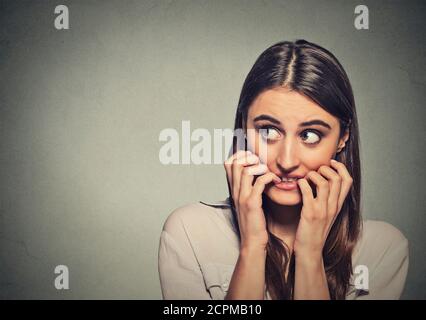 Closeup Portrait junge unsicher zögerlich nervös Frau beißen ihre Fingernägel verlangen nach etwas oder ängstlich, isoliert auf graue Wand Hintergrund. Negati Stockfoto