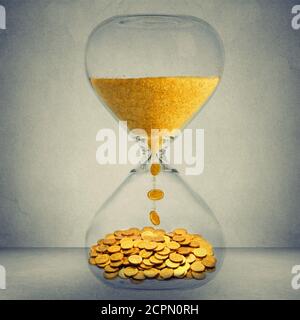 Zeit ist Geld finanzielle Gelegenheit Konzept. Sanduhr mit Goldstaub und Münzen isoliert auf grauem Wandhintergrund Stockfoto