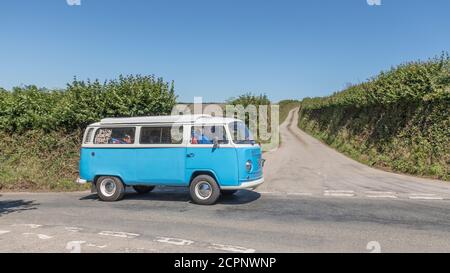 Blau und weiß klassischer VW-Wohnmobil auf sonniger Cornwall Landstraße im Hochsommer (möglicherweise Urlauber). Für Aufenthalte in Großbritannien, Feiertage in Cornwall. Stockfoto