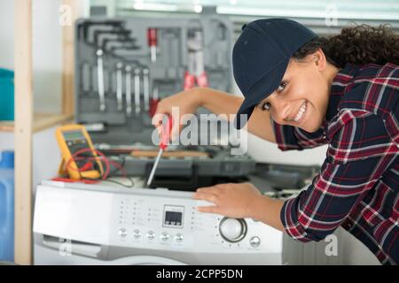 Glückliche Klempnerin, die an der Waschmaschine arbeitet Stockfoto