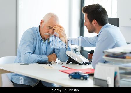 Traurige ältere Angestellte und jüngere, die im Büro sprechen Stockfoto