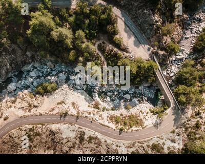 Kurvenreiche Straße und schmale Steinbrücke über eine klare Bergbach in den Asco-Bergen von Korsika Stockfoto