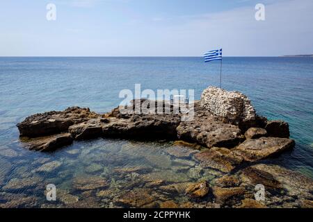 Marathopoli, Messenia, Peloponnes, Griechenland - EINE Taverne im Fischerdorf Marathopoli bietet einen romantischen Tisch unter einer griechischen Flagge auf einem Felsen in Stockfoto