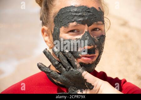 Junge schöne Mädchen mit einem grauen magnetischen Schlamm Maske auf ihrem Gesicht auf einem weißen Hintergrund Stockfoto