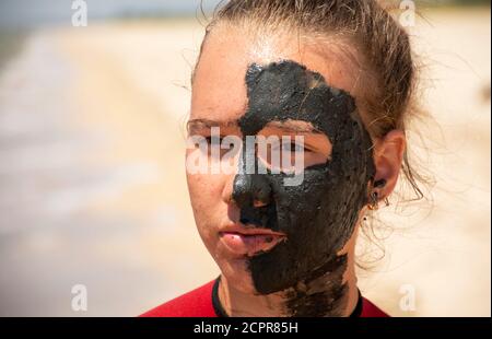 Junge schöne Mädchen mit einem grauen magnetischen Schlamm Maske auf ihrem Gesicht auf einem weißen Hintergrund Stockfoto