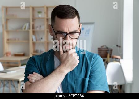 Nachdenklicher junger Geschäftsmann trägt eine Brille und denkt über Problemlösung nach Stockfoto