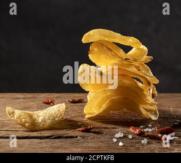 Ein Stapel knuspriger Kartoffelchips auf dunklem Holz mit getrocknetem Cayennepfeffer und Meersalz. Stockfoto