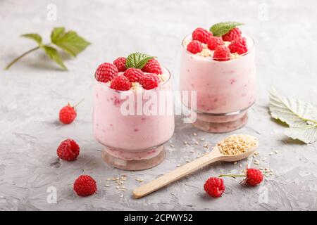 Joghurt mit Himbeere und Sesam in Glas und Holzlöffel auf grauem Betongrund. Seitenansicht, Nahaufnahme. Stockfoto