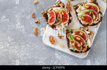 Toast mit Feigen, Käse, Honig, Kräutern und Nüssen. Köstliches Frühstück auf Whiteboard Blick von oben. Gesunde Ernährung Konzept. Stockfoto