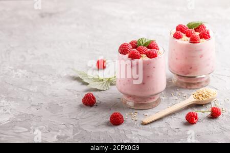 Joghurt mit Himbeere und Sesam in Glas und Holzlöffel auf grauem Betongrund. Seitenansicht, Kopierraum, selektiver Fokus. Stockfoto