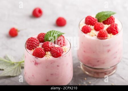 Joghurt mit Himbeere und Sesam in Glas und Holzlöffel auf grauem Betongrund. Seitenansicht, Nahaufnahme. Stockfoto