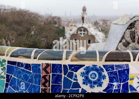 Barcelona, Park Güell, Bank mit zerbrochener Keramik dekoriert, Porter's Lodge im Hintergrund Stockfoto