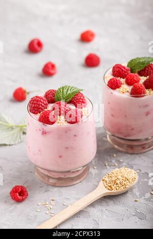 Joghurt mit Himbeere und Sesam in Glas und Holzlöffel auf grauem Betongrund. Seitenansicht, Nahaufnahme. Stockfoto