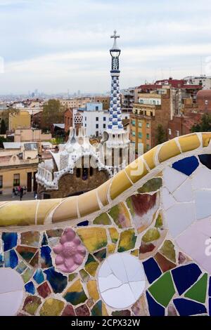 Barcelona, Park Güell, Bank mit zerbrochener Keramik, im Hintergrund Porter's Lodge mit Turm dekoriert Stockfoto