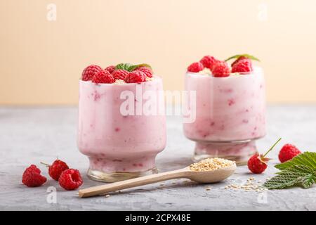 Joghurt mit Himbeere und Sesam in Glas und Holzlöffel auf grauem und orangefarbenem Hintergrund. Seitenansicht, Nahaufnahme. Stockfoto