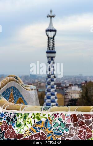 Barcelona, Park Güell, Bank mit zerbrochenen Keramiken, im Hintergrund Turm der Portier-Lodge dekoriert Stockfoto