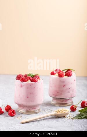 Joghurt mit Himbeere und Sesam in Glas und Holzlöffel auf grauem und orangefarbenem Hintergrund. Seitenansicht, Nahaufnahme. Stockfoto