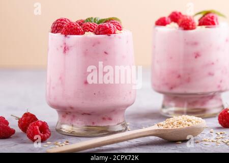 Joghurt mit Himbeere und Sesam in Glas und Holzlöffel auf grauem und orangefarbenem Hintergrund. Seitenansicht, Nahaufnahme. Stockfoto