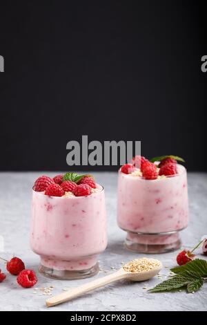 Joghurt mit Himbeere und Sesam in Glas und Holzlöffel auf grauem und schwarzem Hintergrund. Seitenansicht, Nahaufnahme. Stockfoto