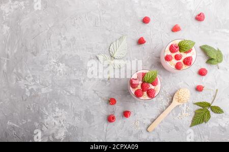 Joghurt mit Himbeere und Sesam in Glas und Holzlöffel auf grauem Betongrund. Draufsicht, flach liegend, Kopierraum. Stockfoto