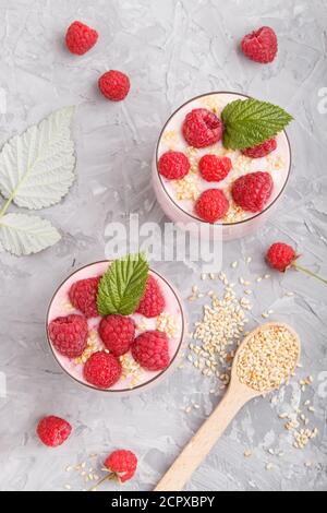 Joghurt mit Himbeere und Sesam in Glas und Holzlöffel auf grauem Betongrund. Draufsicht, flach liegend, Nahaufnahme. Stockfoto